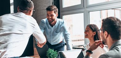 A professional team meeting in a bright office space, featuring individuals shaking hands and smiling, symbolizing collaboration and partnership.