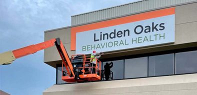 Workers installing a Linden Oaks Behavioral Health sign using a cherry picker lift, ensuring visibility and professional placement.